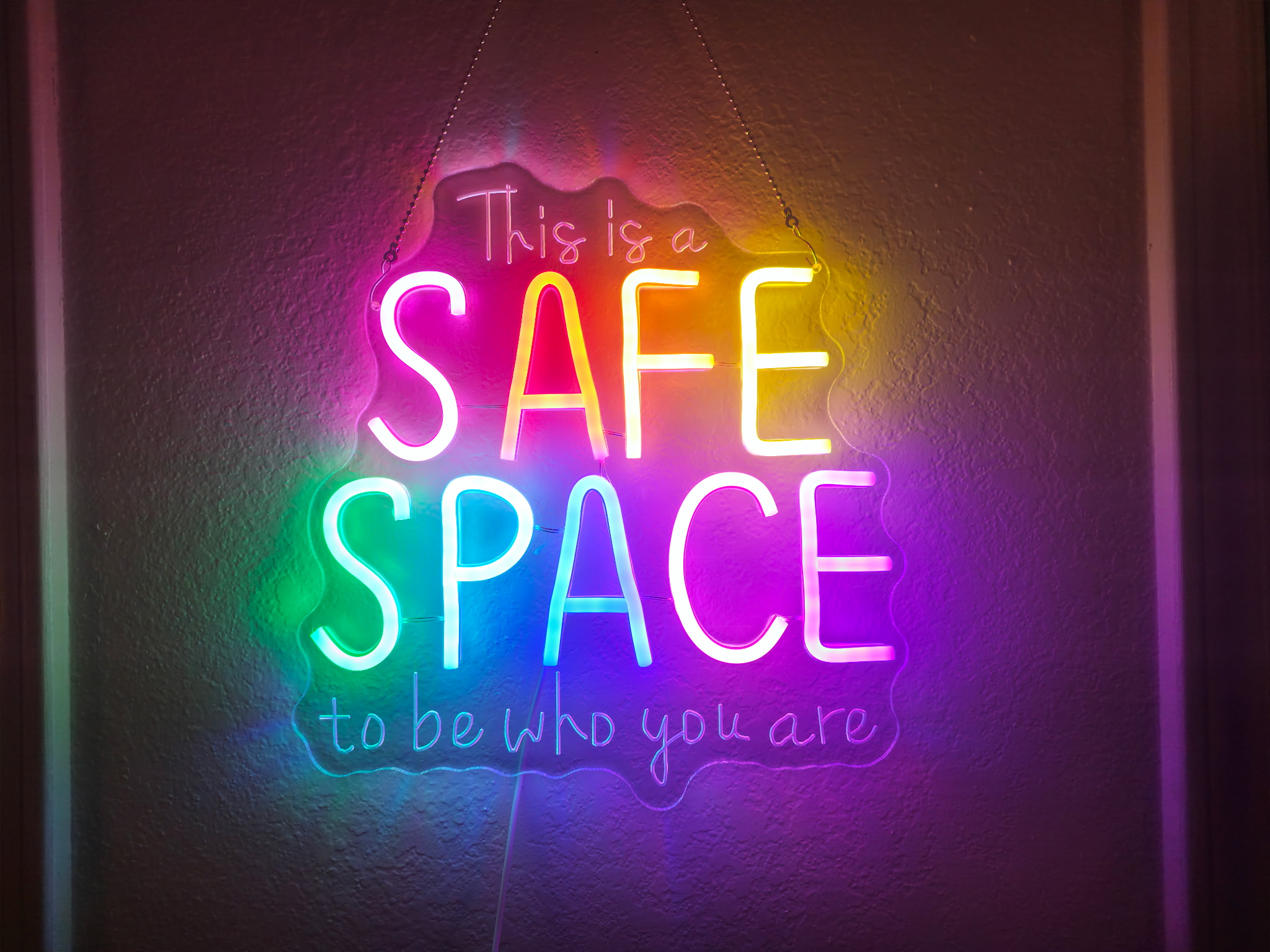 Neon wall sign reading: This is a safe space to be who you are